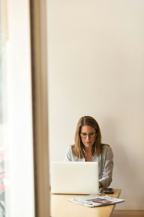 woman-wearing-grey-striped-dress-shirt-sitting-down-near-brown-wooden-table-in-front-of-white-laptop-computer-wS73LE0GnKs.jpg